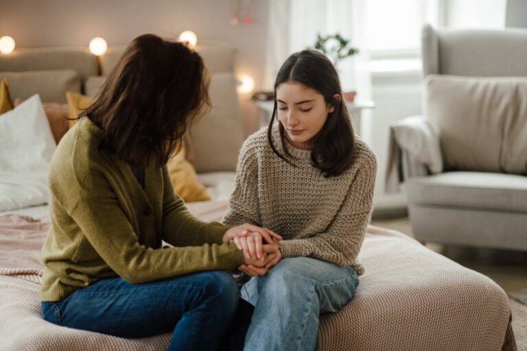 Teenage girl and mother talking in a room, while holding hands.