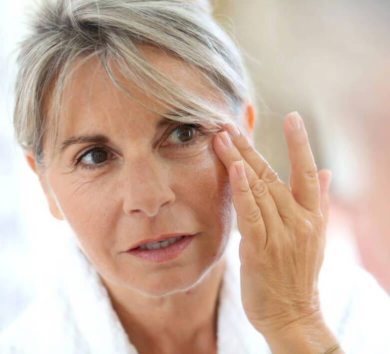 senior woman face with freckles touching skin by hand